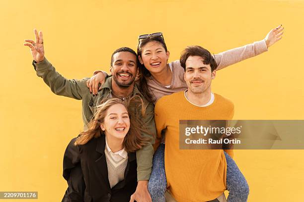 four happy friends smiling and having fun against yellow wall - four people stock pictures, royalty-free photos & images
