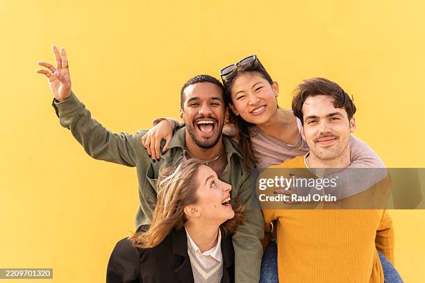 four young adults making funny faces and gestures in front of yellow wall - vier personen stock-fotos und bilder