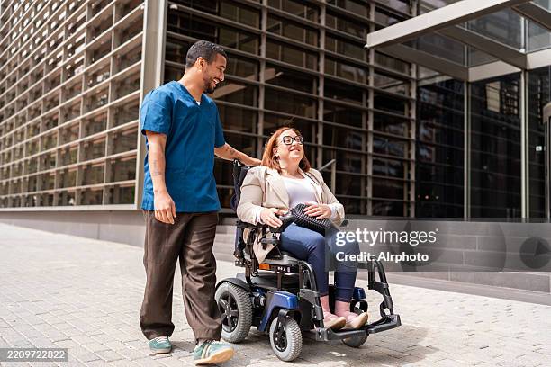 nurse walking a happy patient in a wheelchair outside hospital - rechten van personen met een handicap stockfoto's en -beelden
