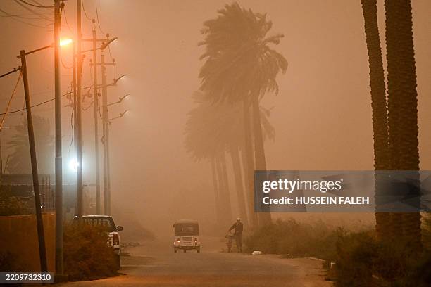 Man pushes a bicycle past a moving tuktuk along a road in low visibility conditions amdist a massive dust storm in Iraq's southern city of Basra on...