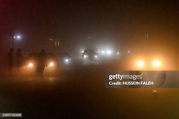 Vehicles move along a road in low visibility conditions amidst a massive dust storm in Iraq's southern city of Basra on April 14, 2025. Around 1,500...