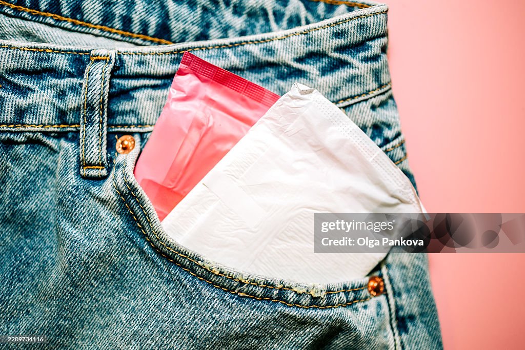 Menstrual pads in pocket of jeans on pink background