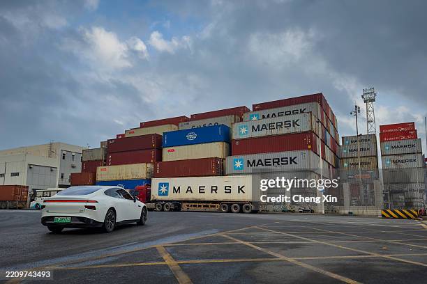 White electric car drives past stacked Maersk shipping containers at a logistics yard near Yantian International Container Terminals, one of China's...