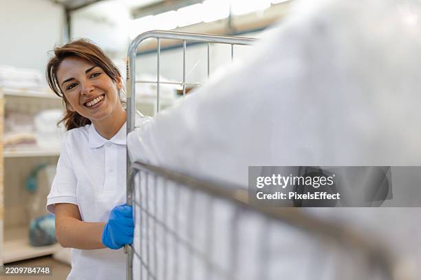 smiling laundry worker in industrial facility with clean linens - laundromat stock pictures, royalty-free photos & images