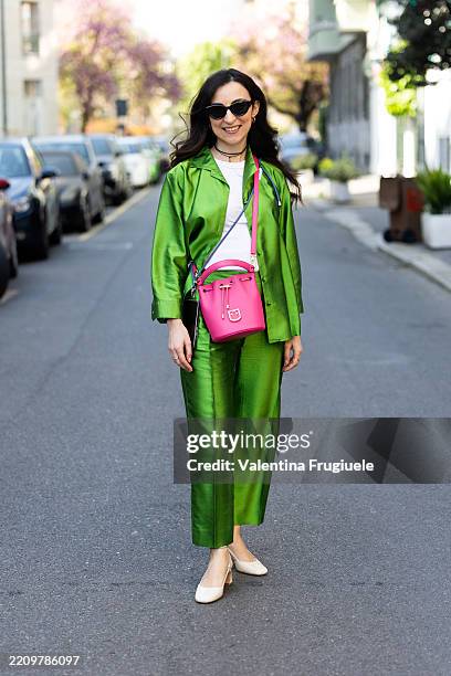 Passerby wears black sunglasses, a white t-shirt, a pink leather bag, white-heeled slingbacks and a green silk coordinated set during the Milan...