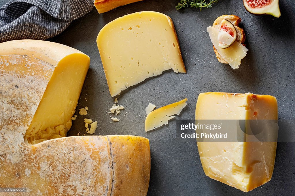 Aged kasar cheese wheel. Cheese wheel. Artisan cheeses.Cheese wheel with bread and fig. Whole wheel of cheese over dark blue background. Whole cheese wheel with wedge slice removed.