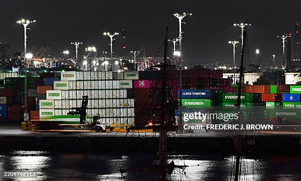 Container trucks make their way past shipping containers stacked high at the Port of Los Angeles on April 14, 2025 in Los Angeles, California....