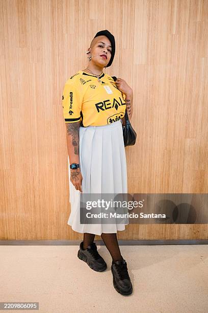 Guest wears yellow soccer jersey, black printed sponsor logos, light blue pleated midi skirt, black sheer tights, chunky black sneakers, black...