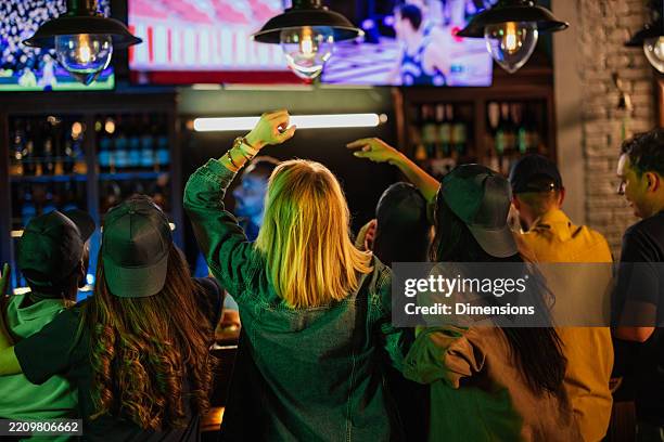 excited friends cheering while watching sports in a pub - sports bar stock pictures, royalty-free photos & images