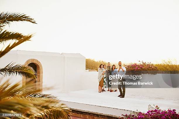 wide shot man taking selfie with friends on rooftop during sunset - clase alta fotografías e imágenes de stock