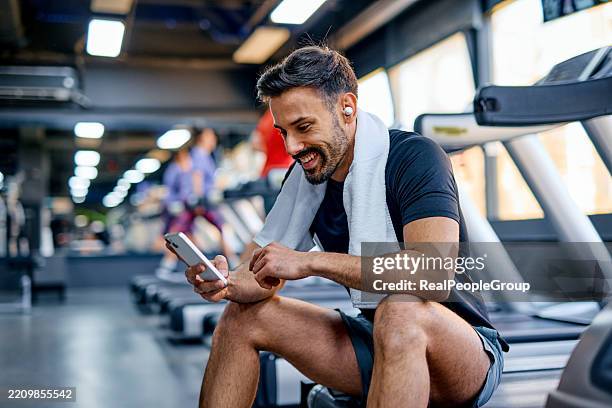 deportista sonriente revisando su teléfono después de entrenar en el gimnasio - centro de bienestar fotografías e imágenes de stock