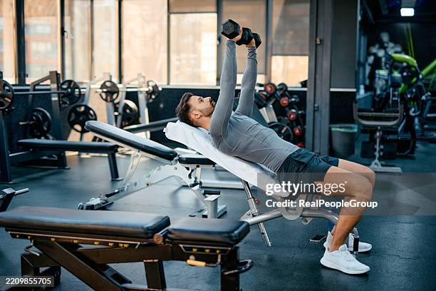 determined sportsman lifting dumbbells while lying on bench in gym - weight bench stock pictures, royalty-free photos & images