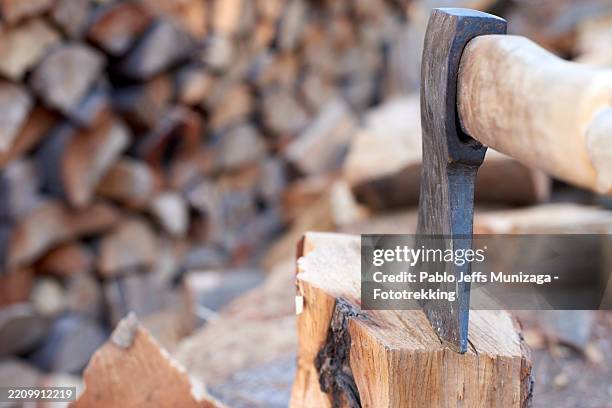 sharp axe splitting wooden log near blurred lumber stack, creating rustic winter preparation scene with raw forestry work and seasonal firewood gathering - chopping wood stock pictures, royalty-free photos & images