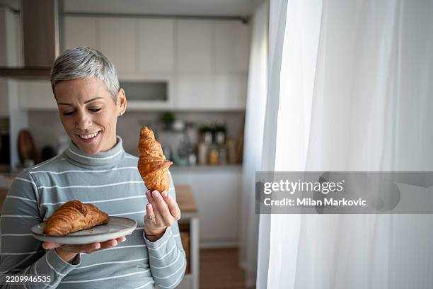 mujer sosteniendo dos croissants y sonriendo en una cocina - carbohidrato fotografías e imágenes de stock
