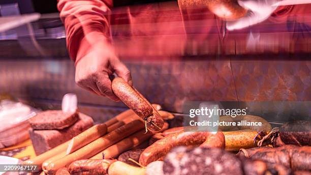 April 2025, Brandenburg, Cottbus: The hand of a vendor takes a sausage from the display on a trolley at a weekly market. Photo: Frank...