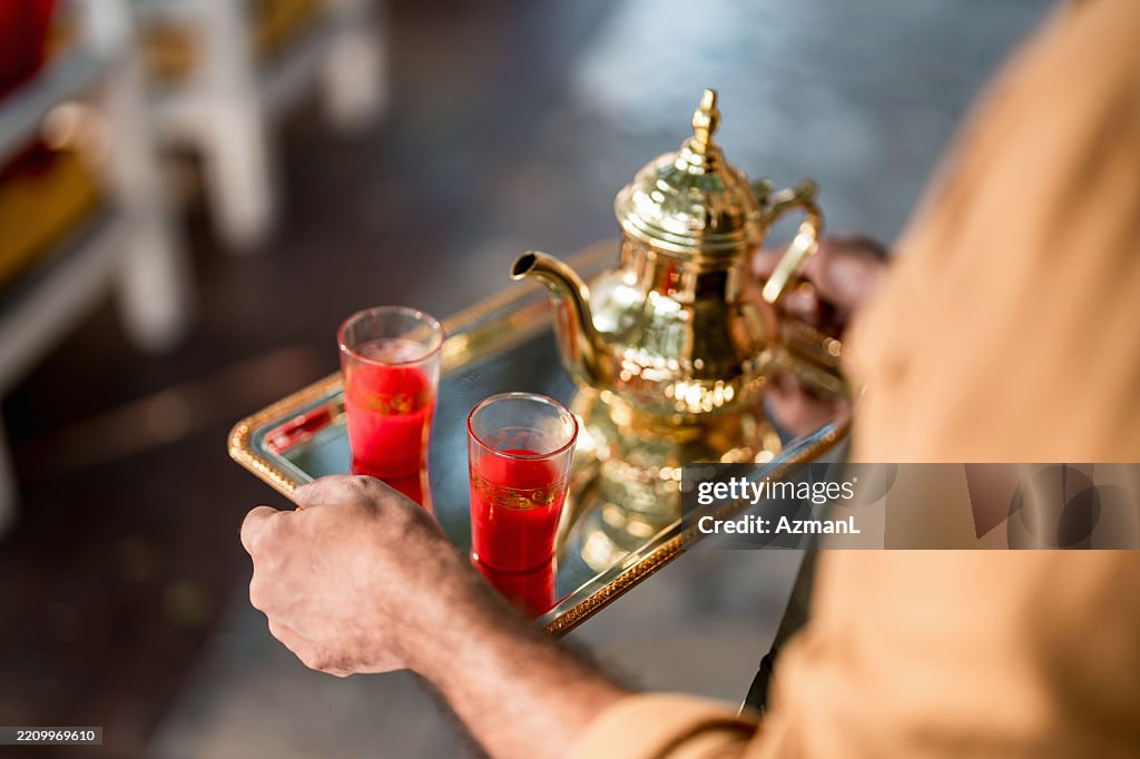 Middle Eastern Cafe Owner Carrying Traditional Brass Teapot On Serving Tray