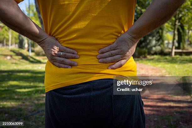 senior man suffering from back pain while exercising in a park, holding his lower back with both hands - herniated disc stock pictures, royalty-free photos & images