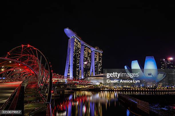 View of the Helix Bridge, Marina Bay Sands and the ArtScience Museum are illuminated at night, casting vibrant reflections on the water at Marina Bay...