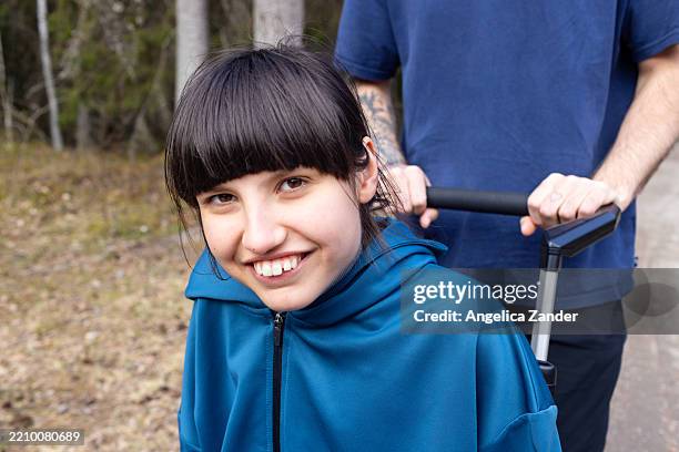 portrait of happy teenage girl in wheelchair enjoying nature walk with family - developmental disability stock pictures, royalty-free photos & images