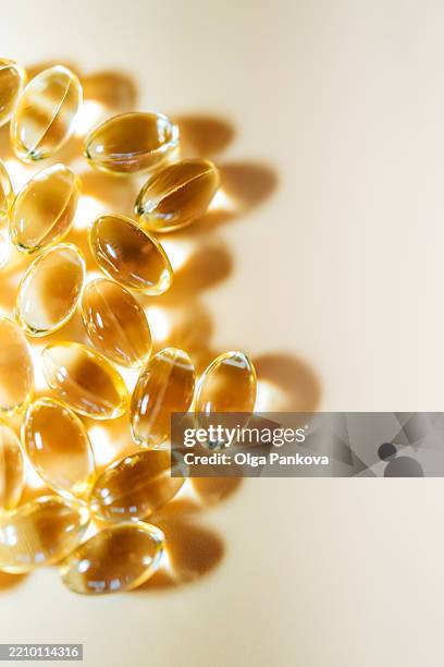 softgels with transparent yellow oily substance reflecting sunlight on beige background - vitamine d stockfoto's en -beelden