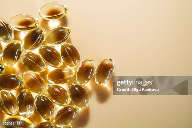softgels with transparent yellow oily substance reflecting sunlight on beige background - vitamine d stockfoto's en -beelden