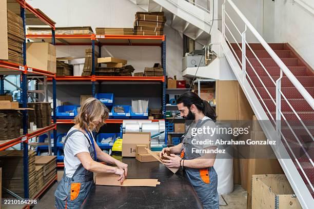 warehouse workers sorting cardboard boxes, organizing packaged goods on table for efficient shipping logistics in storage facility - gestión de inventarios fotografías e imágenes de stock