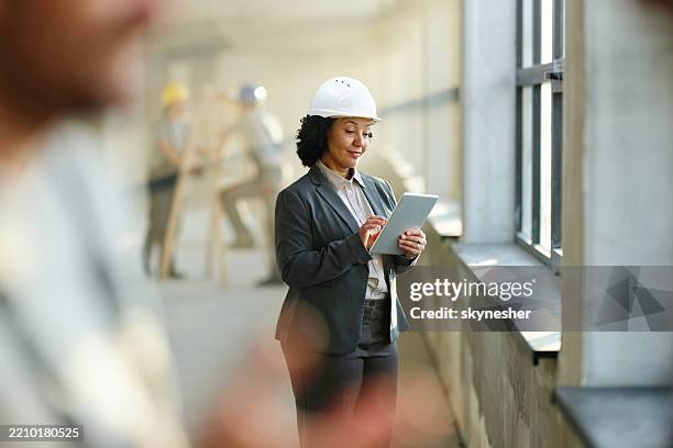 smiling female building contractor working on touchpad at rebuilding site. - bygghjälm bildbanksfoton och bilder