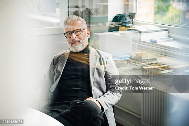 portrait of a senior male professional sitting alone by an office window - weißes haar stock-fotos und bilder