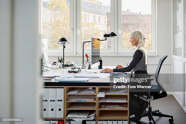 a focused female architect works at her organised desk in a modern office - one mature woman only stock pictures, royalty-free photos & images