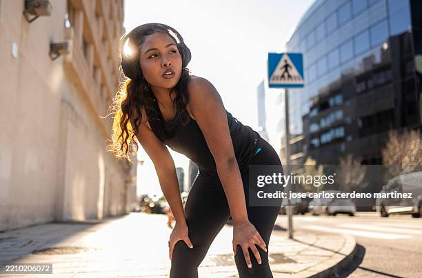 young sporty woman taking a break during her outdoor workout in the city - hand op knie stockfoto's en -beelden