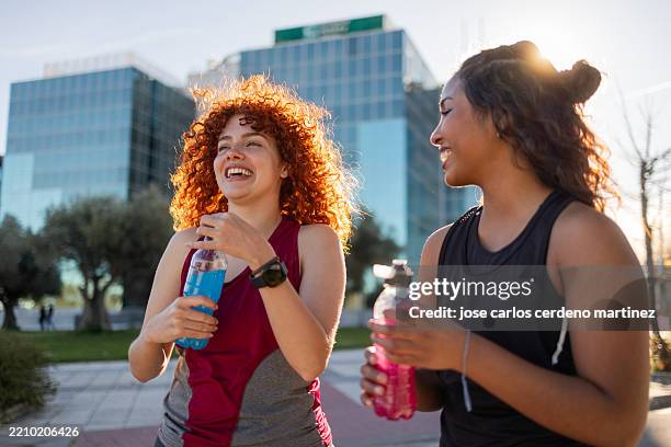 two young women drinking refreshing drinks after workout in the city - energydrink stock-fotos und bilder