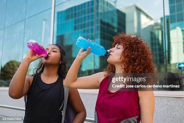 two sporty women drinking energy drink after workout in the city - energydrink stock-fotos und bilder