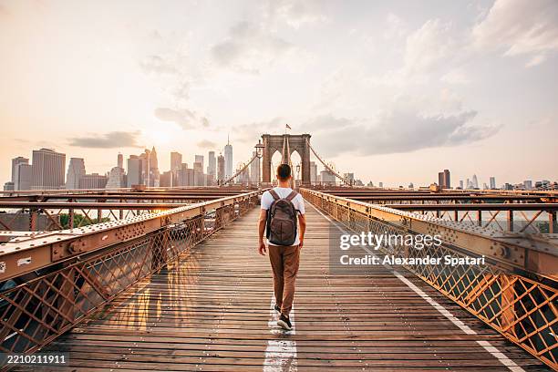 man with backpack walking on brooklyn bridge towards manhattan at sunset, new york city, usa - wonderlust imagens e fotografias de stock