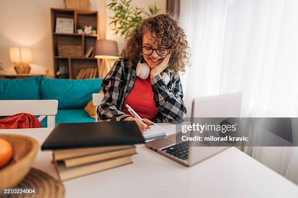 young student taking notes while attending online class at home - attending webinar stock pictures, royalty-free photos & images
