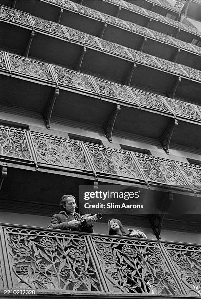 Man holding a camera stands with a woman on the balcony of the Chelsea Hotel in New York City, 1967.