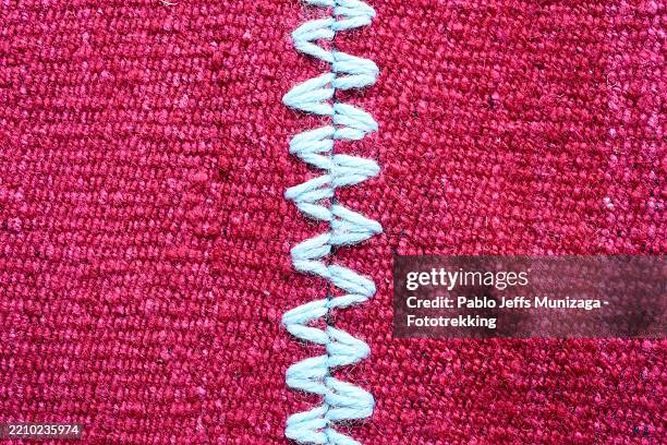 white zigzag overlock stitch running along vivid red textile, revealing precise stitching details and textural intricacies of fabric surface - appliqué stock pictures, royalty-free photos & images