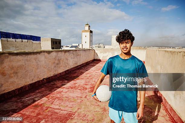 medium wide shot portrait of soccer player holding ball on rooftop - moroccan culture stock pictures, royalty-free photos & images