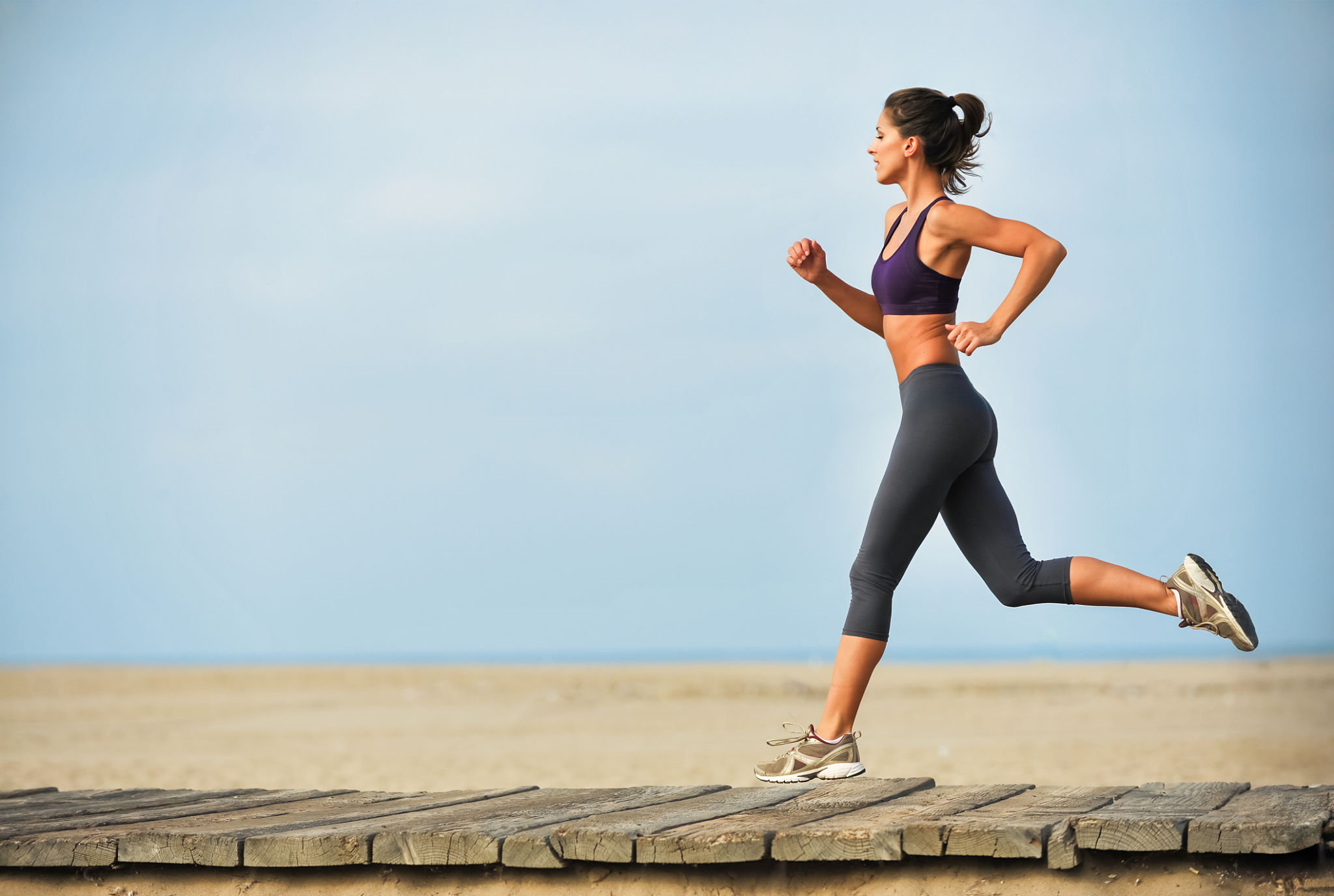Pretty young Caucasian woman running along boardwalk on Santa Monica Beach wearing leggings and sports bra. Pretty young Caucasian woman running along boardwalk on Santa Monica Beach wearing leggings and sports bra.