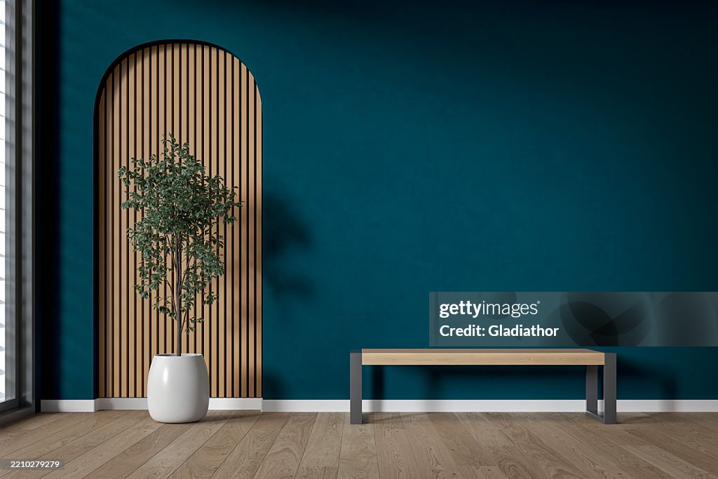 Modern interior: an unfurnished living/waiting room with a modern bench, a potted plant (ficus) in front of a partly textured deep blue wall, partly arched paneled light pink wooden slat, large window and decoration