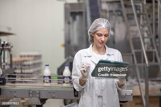 female diary factory supervisor standing in front of conveyor belt and using digital tablet - hair net stock pictures, royalty-free photos & images