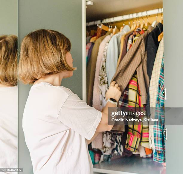 frau wählt kleidung aus ihrem kleiderschrank aus - kleiderschrank stock-fotos und bilder