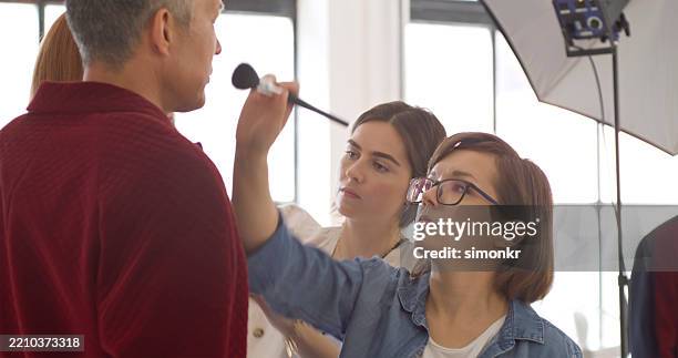 studio behind-the-scenes with diverse team and makeup artist applying touch-up - film set stock pictures, royalty-free photos & images