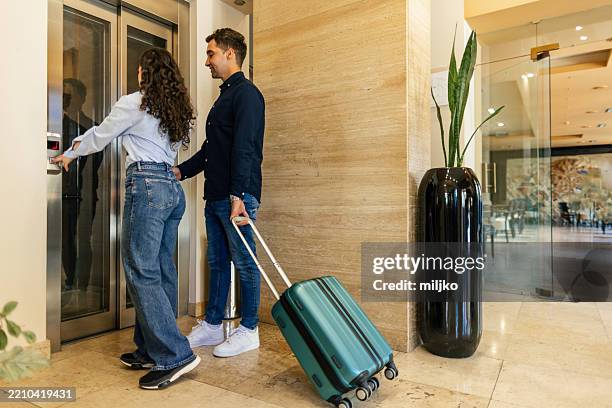 pareja joven esperando ascensor en el hotel con equipaje - motel pareja fotografías e imágenes de stock