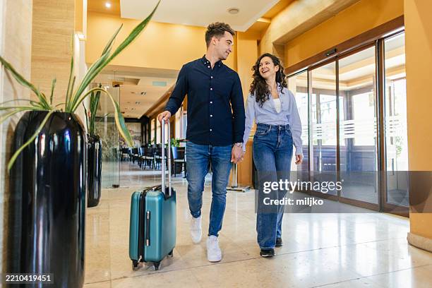 pareja joven entrando en el vestíbulo del hotel para registrarse - motel pareja fotografías e imágenes de stock