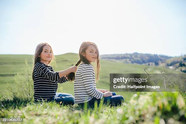 best friends sitting in a meadow, braiding each others hair. - freizeitaktivität im freien stock-fotos und bilder