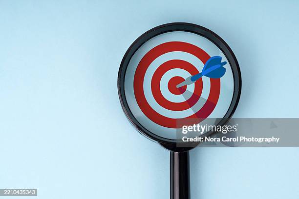 magnifying glass focused on dart and bullseyes - target market stock pictures, royalty-free photos & images