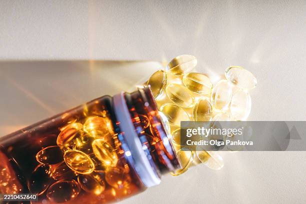 golden vitamin d pills spilling from brown bottle onto brightly lit surface - antiarrugas fotografías e imágenes de stock