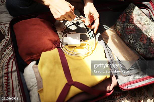 woman in jeans shirt seating on bed and packing travel case, backlit with sun - chargeur de batterie photos et images de collection