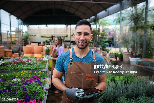 lateinischer gärtner lächelnd und tablette in der hand im gewächshaus - gartenhandschuh stock-fotos und bilder
