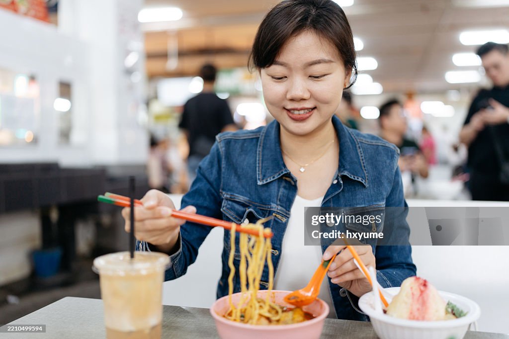 Smiling female tourist is enjoying famous Penang white curry noddle at local morning market